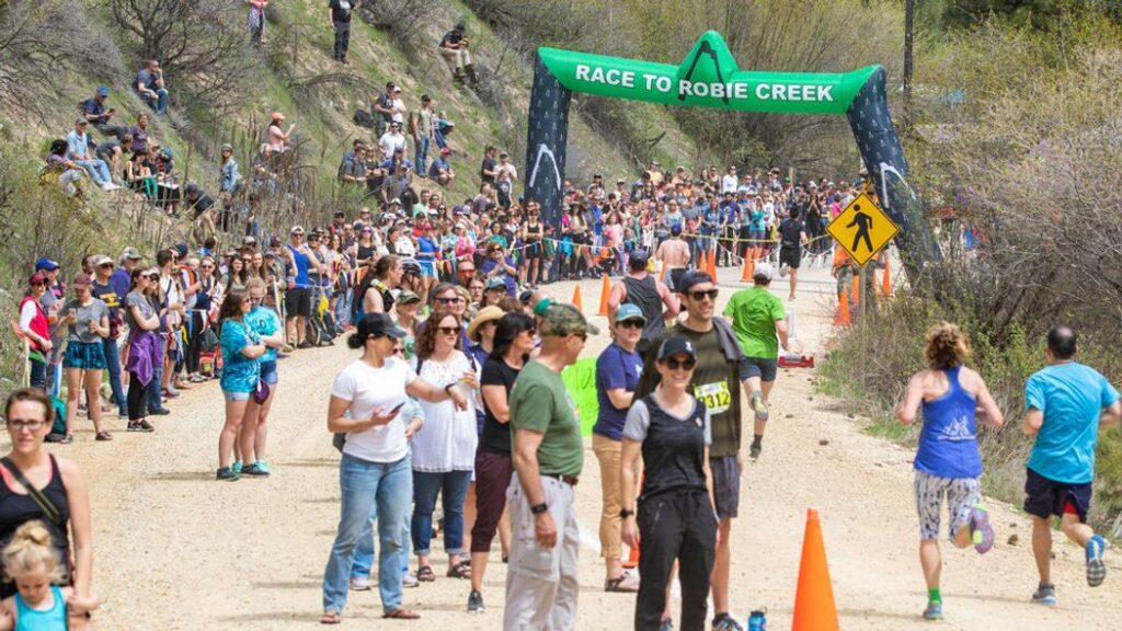 Spectators and runners gather at the finish line of the Race to Robie Creek, with the large inflatable race banner in the background.